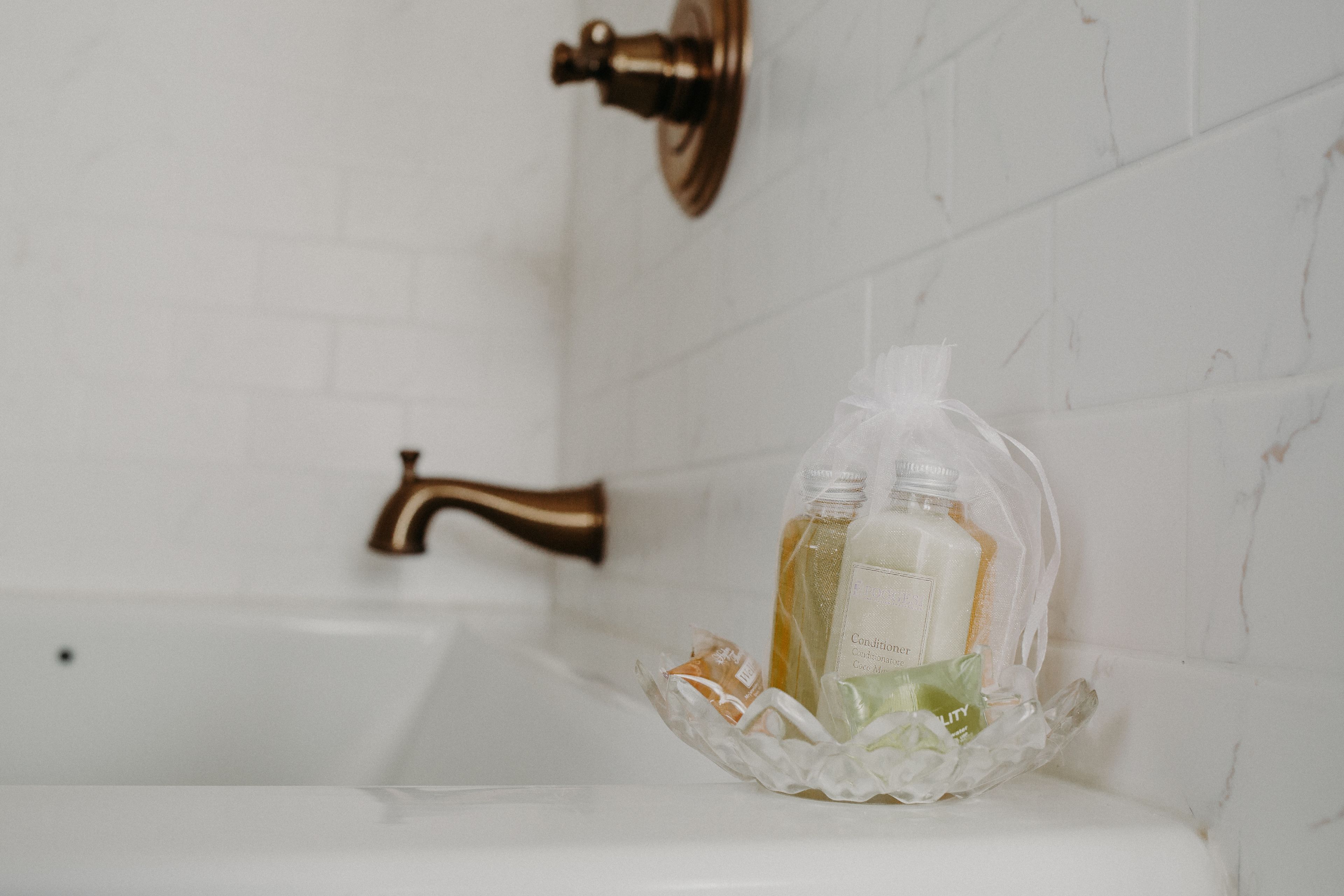 Un baño con una bañera blanca, un grifo de latón y artículos de aseo en una cesta de plástico transparente.