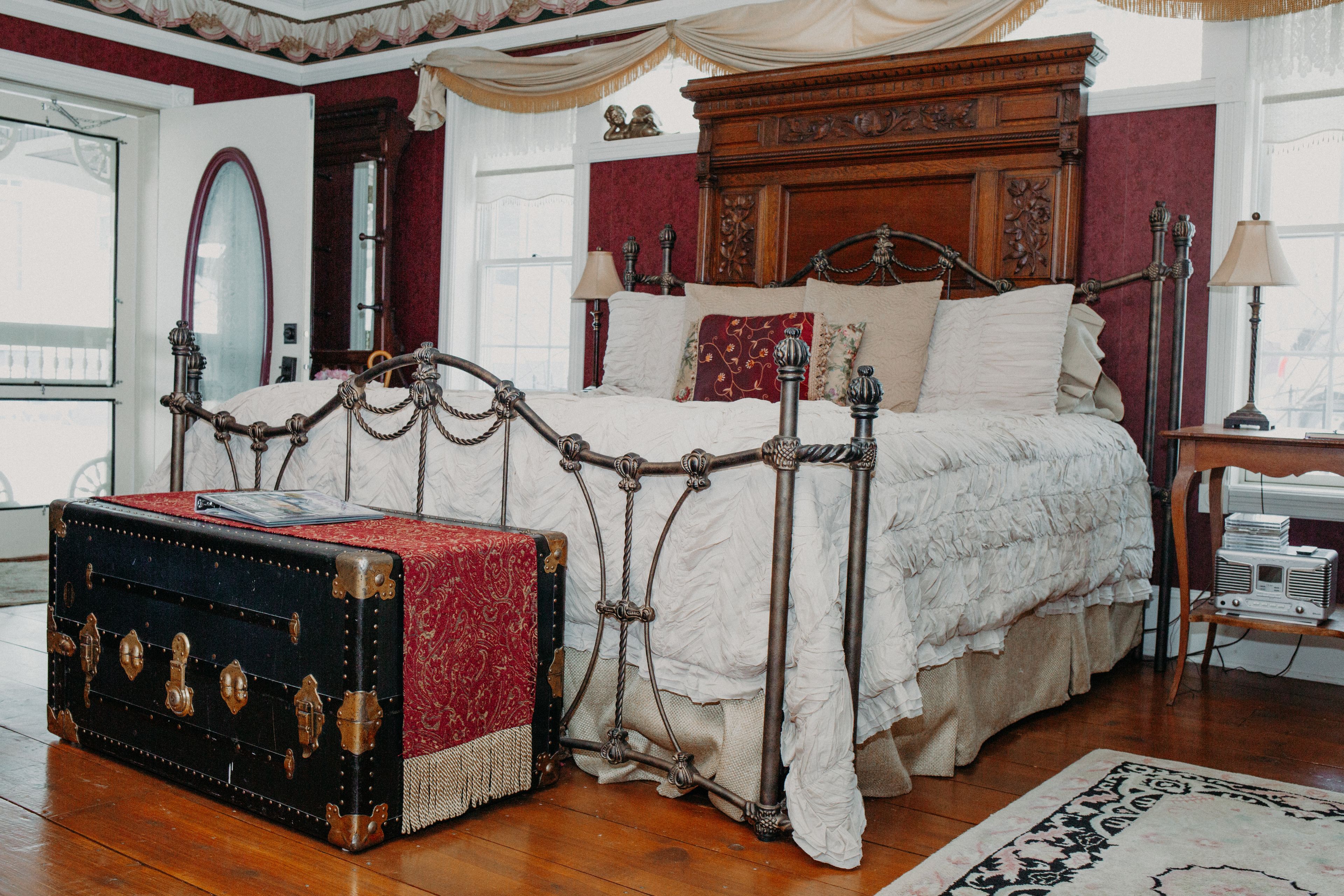 Un dormitorio clásico con una cama con dosel, un baúl antiguo y un espejo grande.