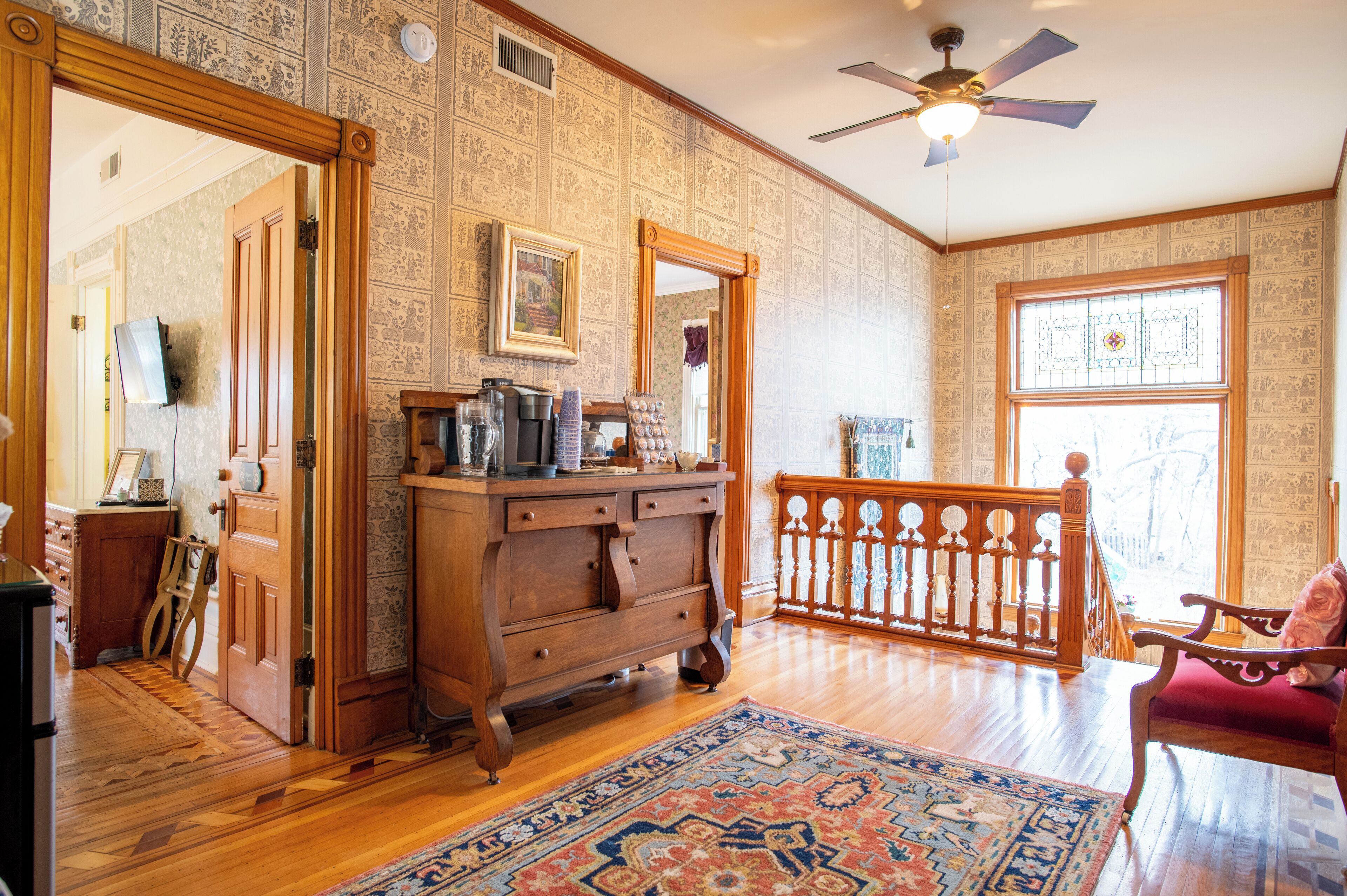 A room with wooden flooring, a large mirror, a ceiling fan, and a wooden railing.
