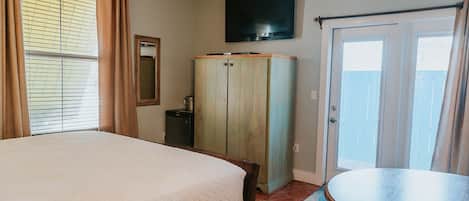 A bedroom with a bed, a wardrobe, a television, and a door leading to a balcony.