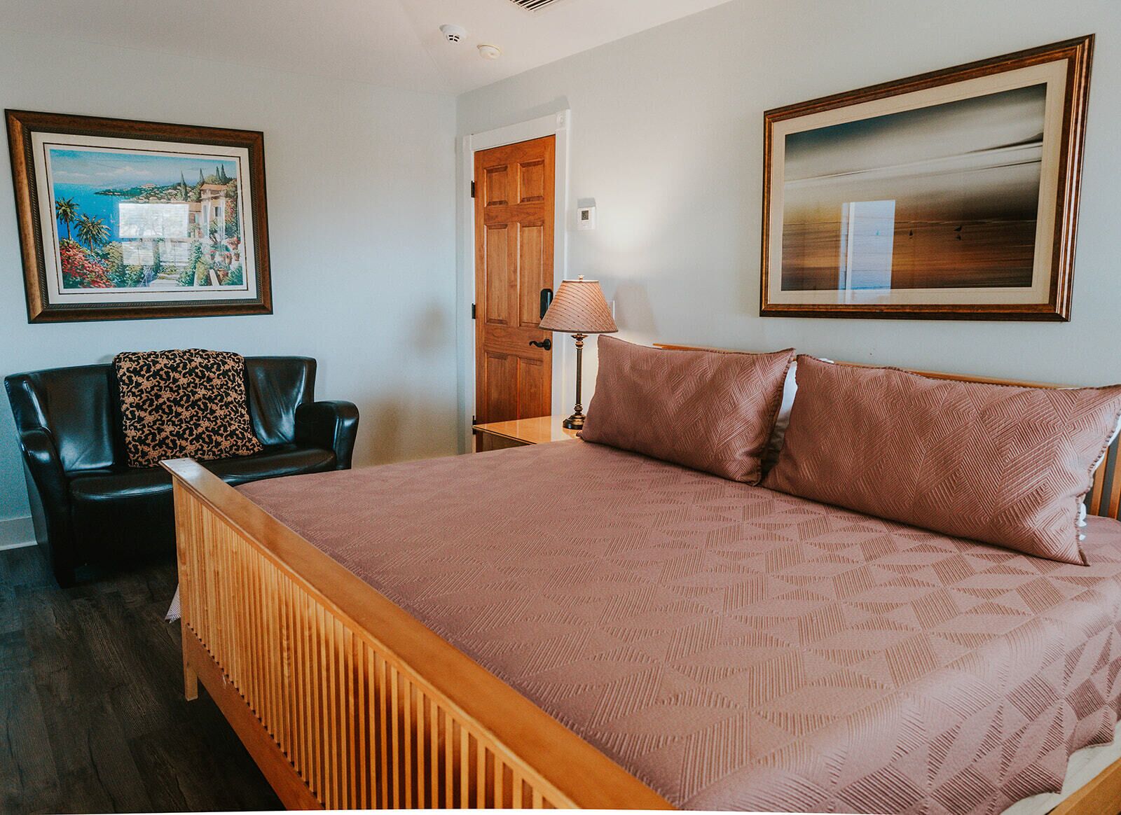 A bedroom with a wooden bed, a black leather chair, a wooden nightstand, and two framed pictures on the walls.