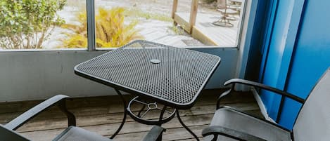 A balcony with a metal table and two chairs, overlooking a dock and water.