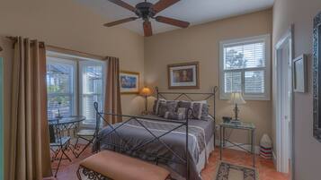 A bedroom with a bed, a ceiling fan, two bedside tables, a bench, and a window with blinds.