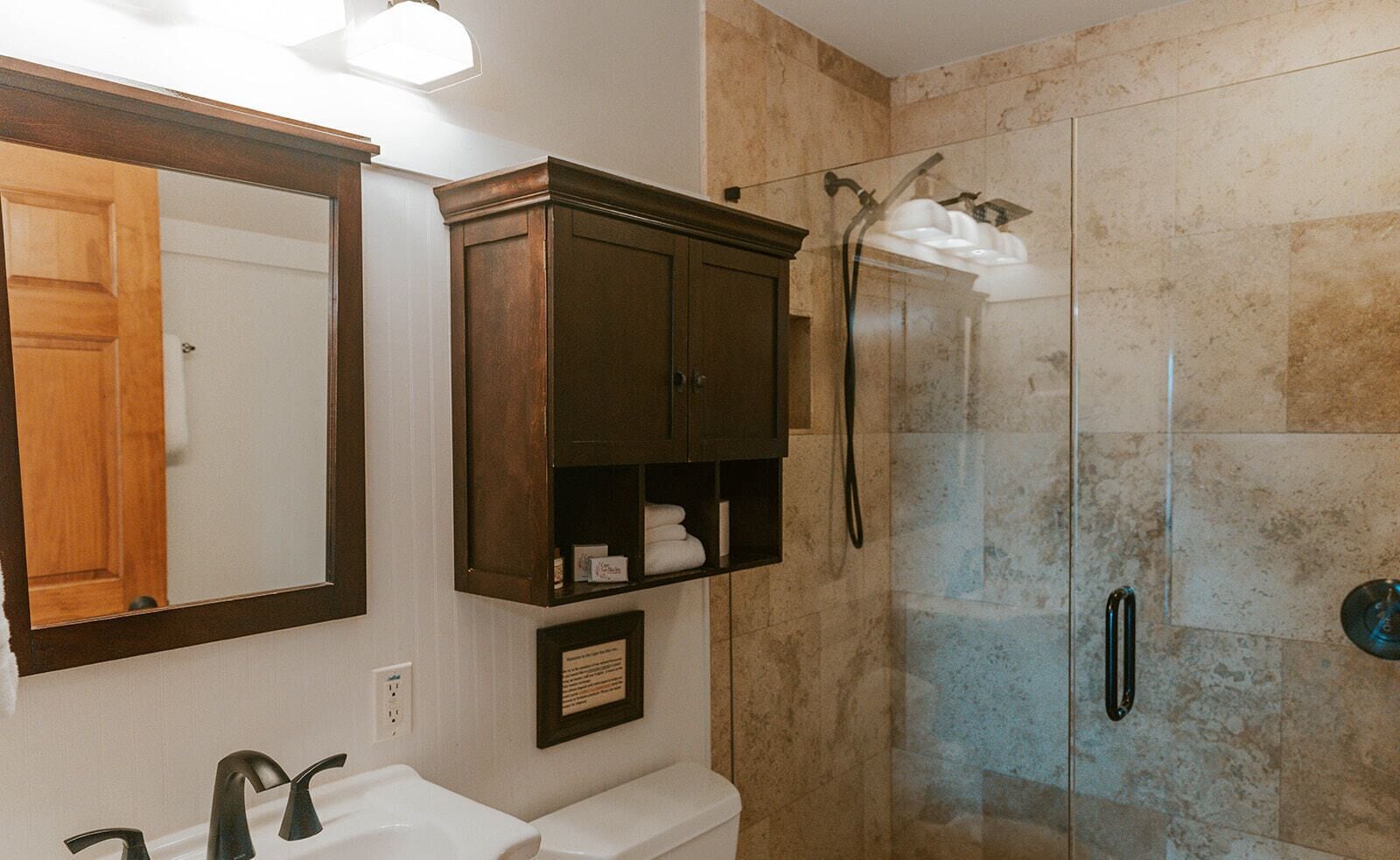 A bathroom with a wooden vanity, a mirror, a framed certificate, and a glass-enclosed shower area.