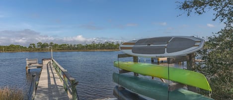 A wooden dock extending into a calm lake, with a green kayak and a white and brown canoe on a stand.