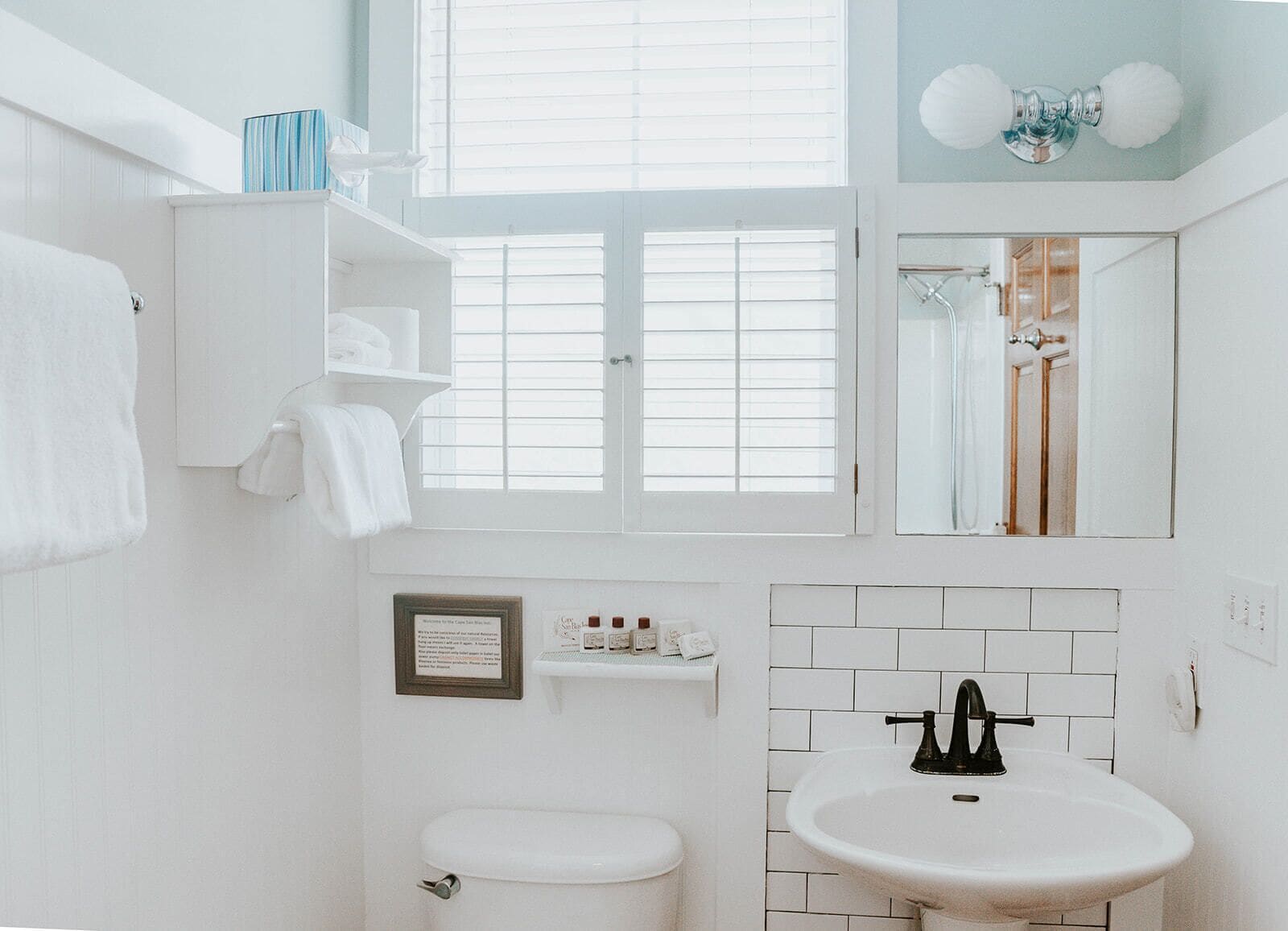 A bathroom with a white toilet, a sink, a mirror, and a window with blinds.