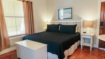 A neatly arranged bedroom with a bed, bedside tables, a nightstand, and a small white desk.