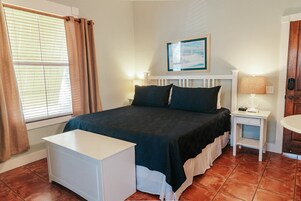 A neatly arranged bedroom with a bed, bedside tables, a nightstand, and a small white desk.