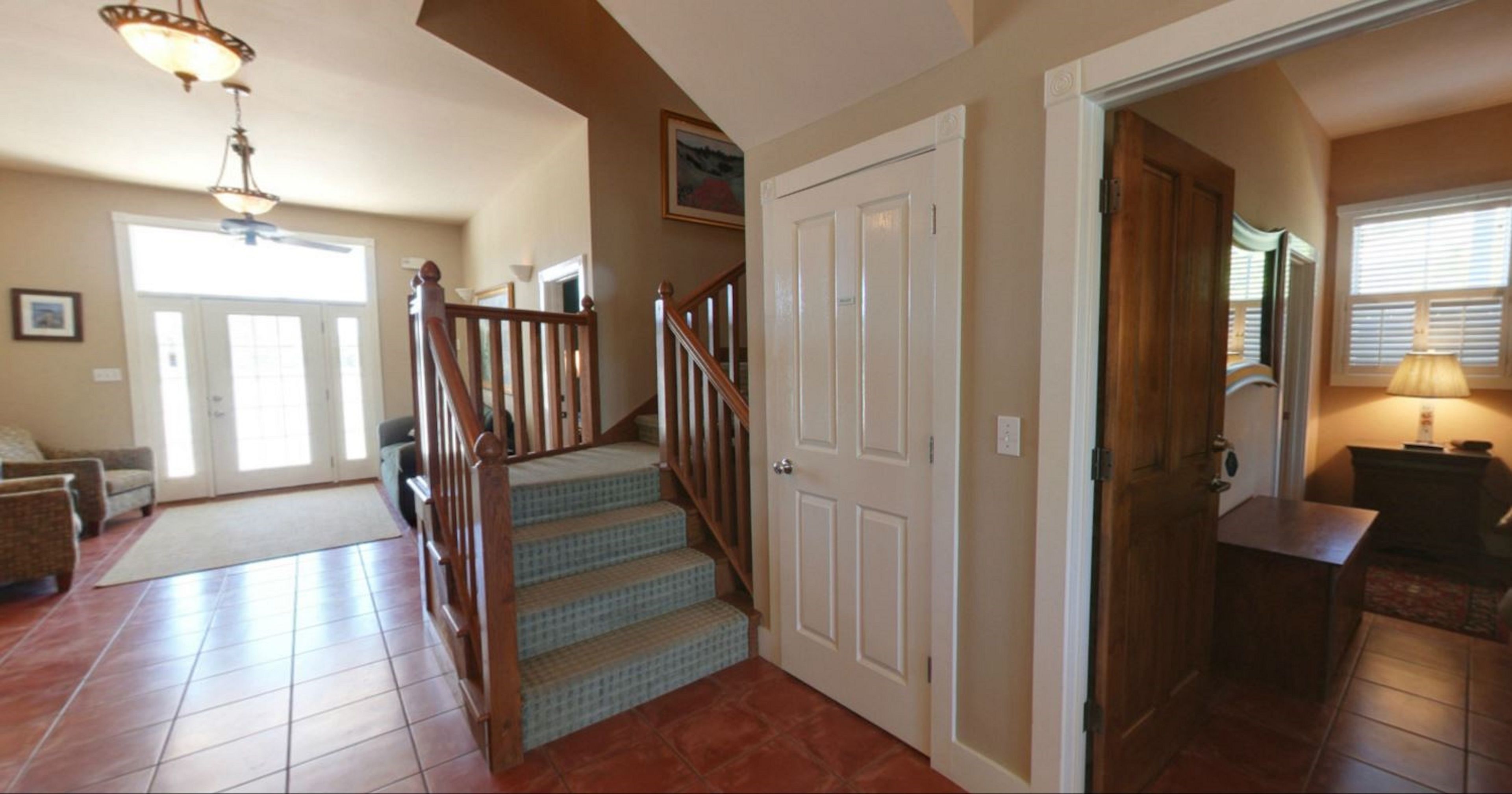 A spacious living area with a staircase, a door leading to another room, and a window with blinds.
