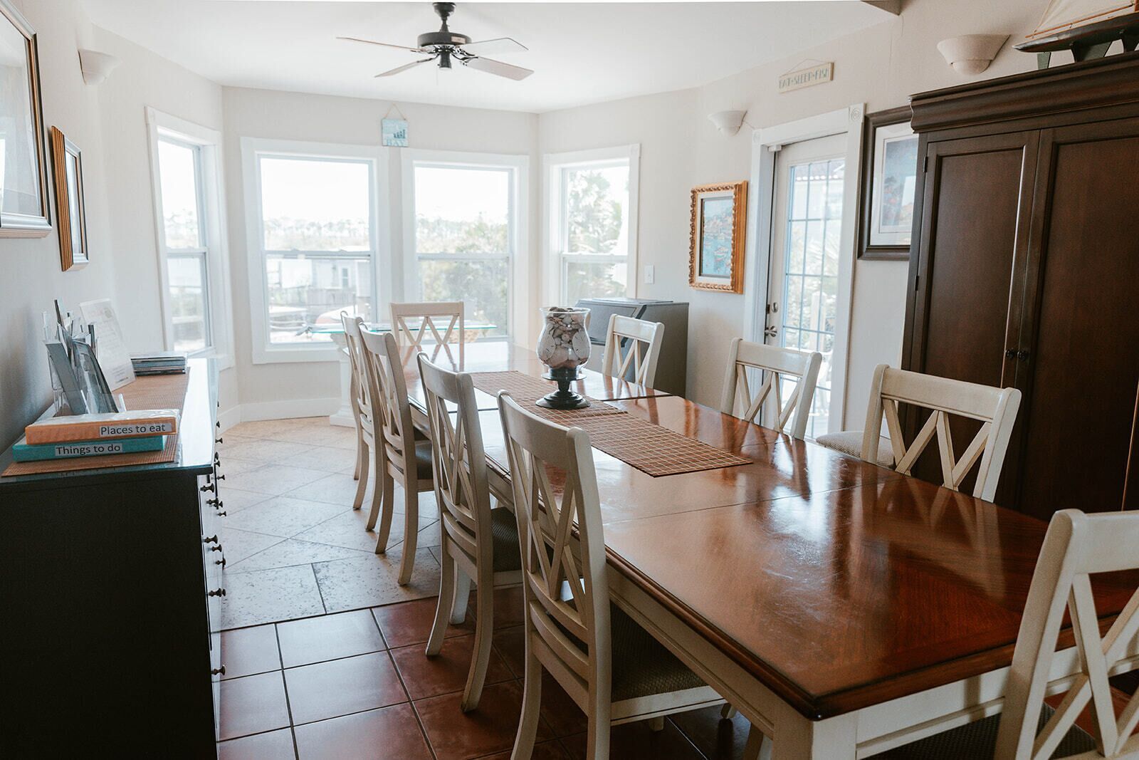 Un coin repas avec une table en bois, des chaises blanches et un ventilateur de plafond.