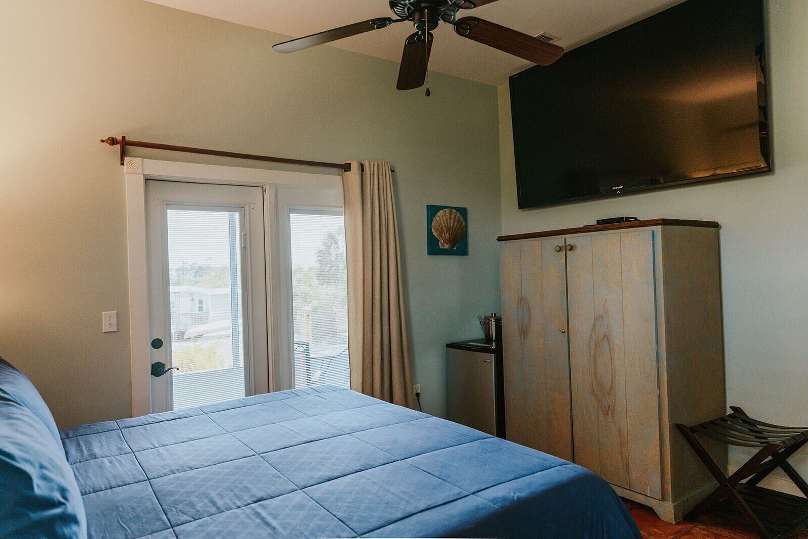 A bedroom with a bed, a ceiling fan, a wardrobe, and a TV mounted on the wall.