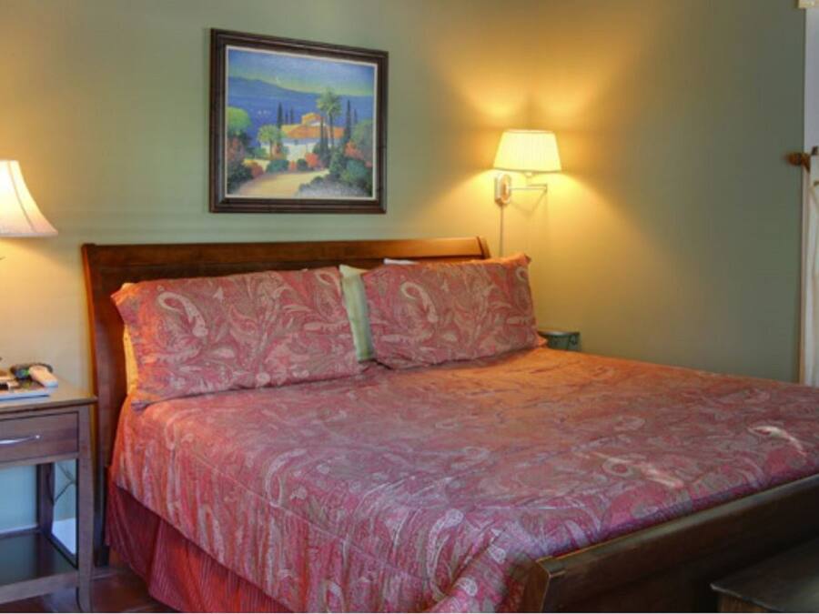 A bedroom with a bed, bedside lamps, a painting on the wall, and a window with blinds.