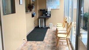 A hallway with a black mat, wooden chairs, a small table, a map on the wall, and a radiator. - Travel Inn (Broadview)