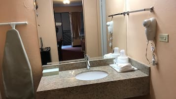 A hotel bathroom with a granite countertop, a sink, a mirror, a hairdryer, and a towel rack.