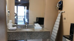 A bathroom with a granite countertop, a sink, a mirror, a towel dispenser, a trash can, and a shower curtain. - Travel Inn (Broadview)