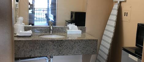 Baño con encimera de granito, lavamanos, espejo, dispensador de toallas, cubo de basura y cortina de ducha.