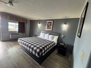 A bedroom with a bed, bedside tables, a window with curtains, a wall-mounted picture, and a ceiling fan.