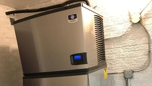 A stainless steel refrigerator with a water dispenser, located in a room with white brick walls and a tiled floor. - Travel Inn (Broadview)