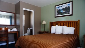 A hotel room with a bed, a desk, a chair, a toilet, and a framed picture on the wall.