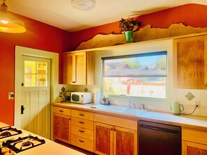 Une cuisine avec des meubles en bois, un four à micro-ondes, un évier et une fenêtre donnant sur un quartier résidentiel.