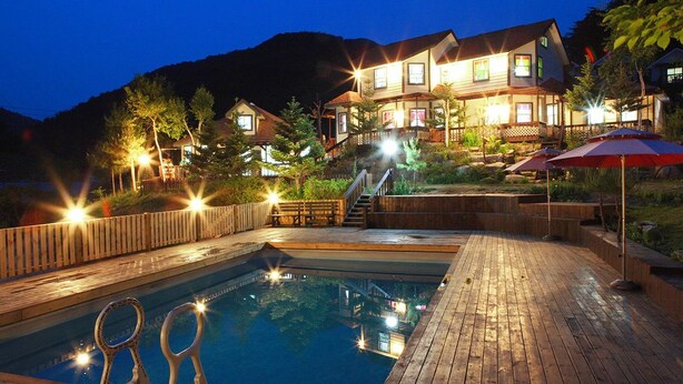 A pool area with a wooden deck, a staircase leading to a building, and outdoor umbrellas. - Duo Pension (Pyeongchang)