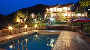 A pool area with a wooden deck, a staircase leading to a building, and outdoor umbrellas. - Duo Pension (Pyeongchang)