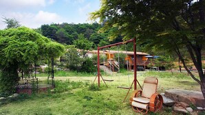 A garden with a swing set, a wicker chair, and a building in the background. - Duo Pension (Pyeongchang)