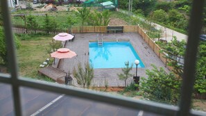 A rectangular swimming pool with a wooden deck, surrounded by a fence and small trees. - Duo Pension (Pyeongchang)