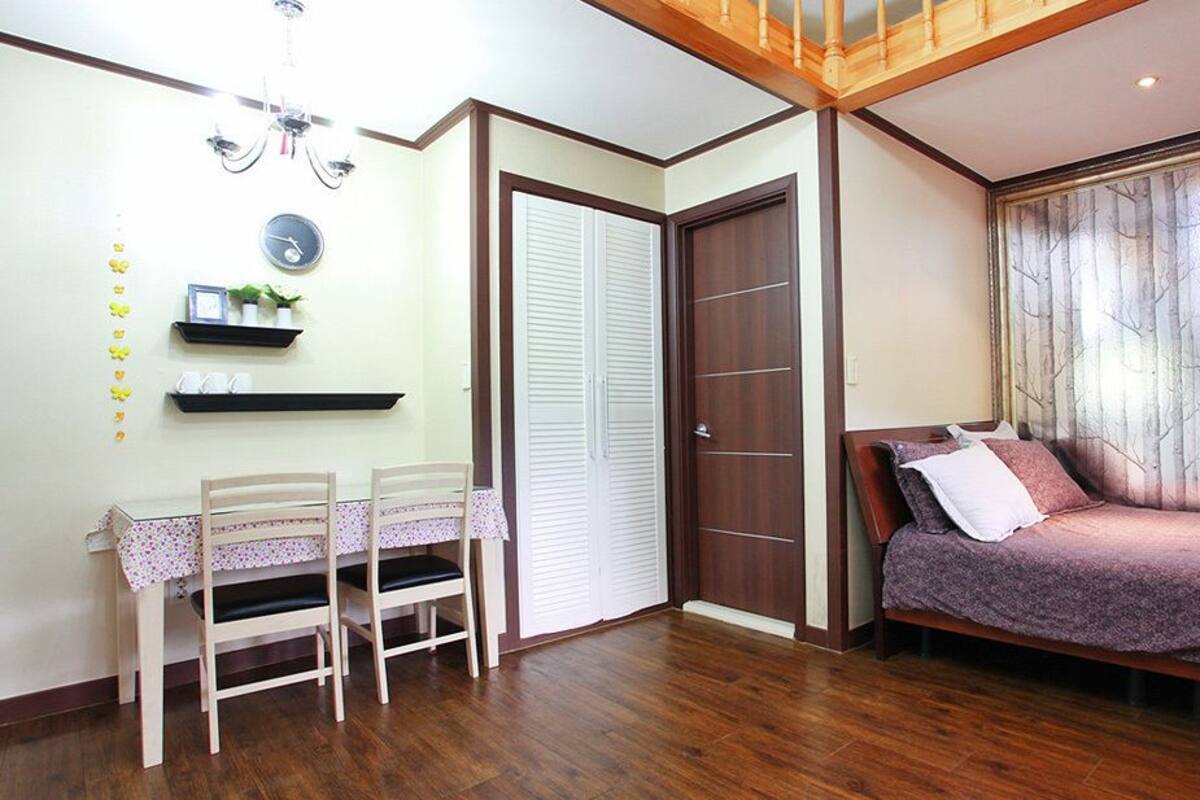 Un dormitorio con cama, un escritorio con sillas, un armario y una ventana con vistas al bosque.