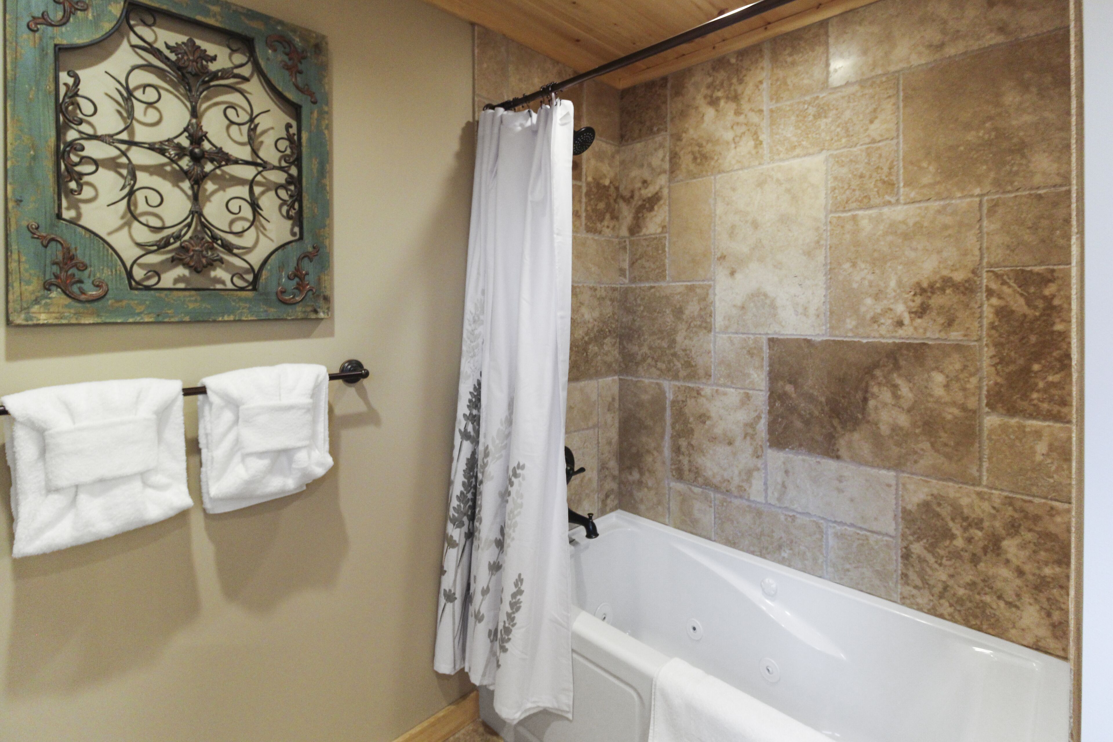 Un baño con bañera, paredes de azulejos color crema y un adorno metálico sobre la barra para toallas.