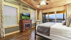A bedroom with a bed, a television, a fireplace, and a balcony with a view.