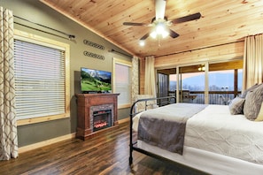 A bedroom with a bed, a television, a fireplace, and a balcony with a view.