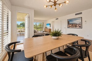 A dining area with a wooden table, black chairs, a potted plant, a television, and a framed picture on the wall.