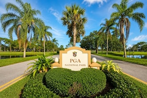 A sign for PGA National Park with a well-maintained lawn and palm trees.