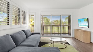 A modern living room with a grey sofa, a round coffee table, and a TV on the wall. - Restoration Hardware PGA National Condo w/ 180° Golf Course Views (Palm Beach Gardens)
