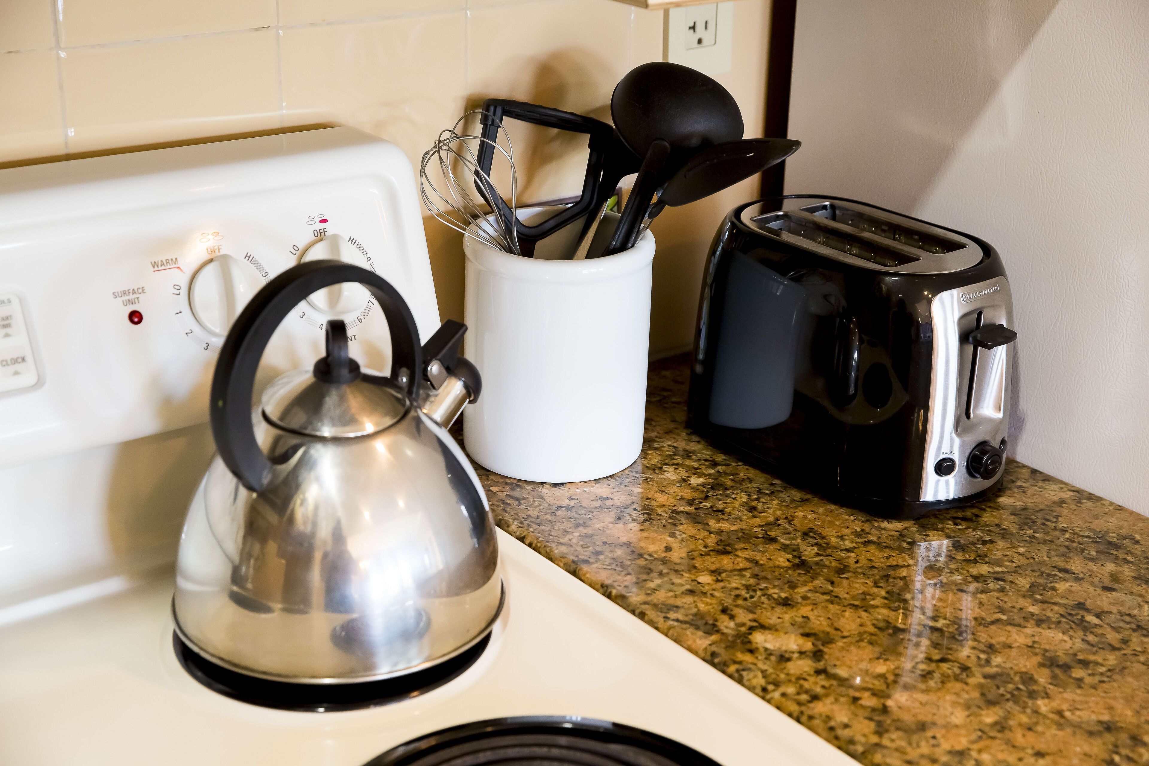 Una cocina con tetera, tostadora y un portalapices sobre una encimera de granito.