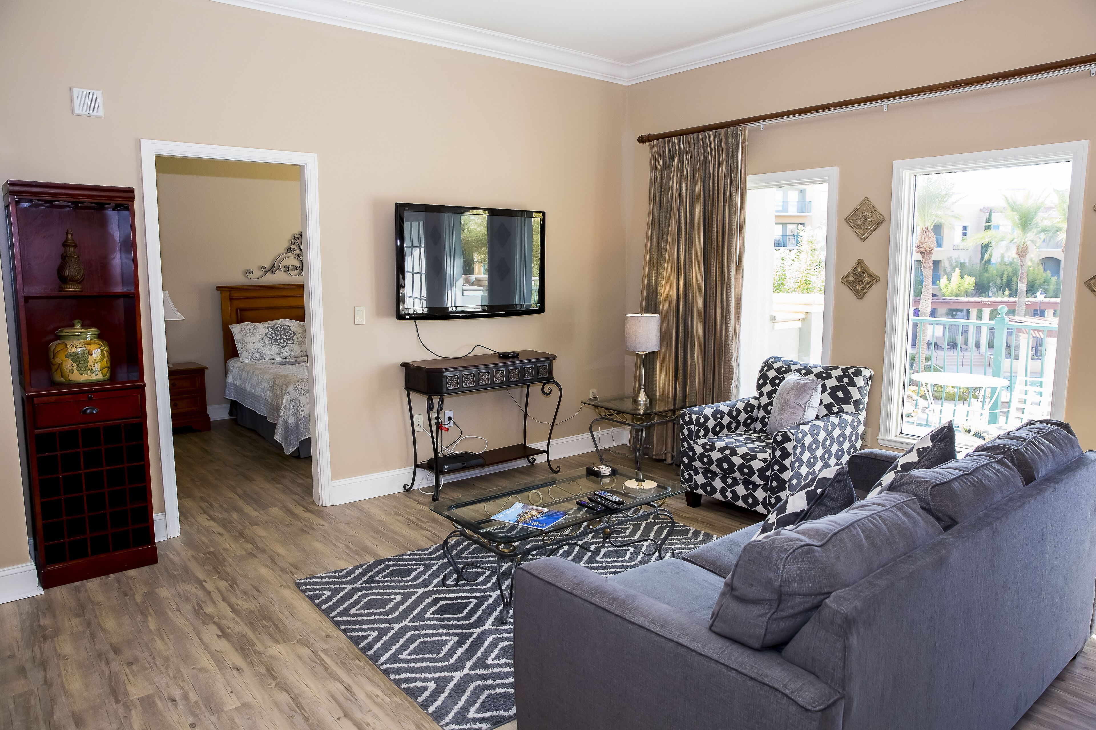 Una sala de estar con un sofá gris, un sillón estampado, un televisor de pantalla plana y un aparador de madera.