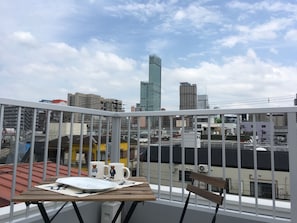 Varanda com uma mesa, dois copos e uma cadeira, com vista para um horizonte urbano com diversos edifícios.