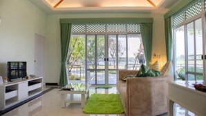 A living room with a sofa, a coffee table, a TV, and a view of the outdoors through large windows. - Tubtim Siam River Kwai Resort (Kanchanaburi)