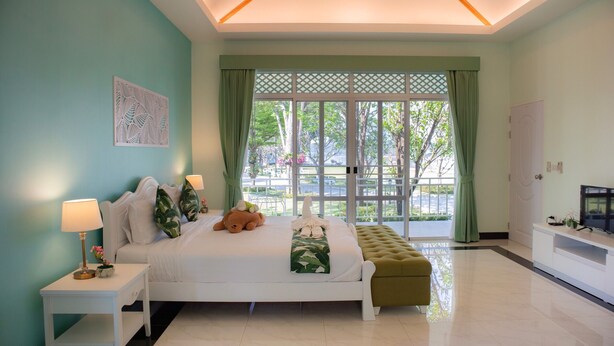 A bedroom with a bed, bedside table, green curtains, and a view of the outdoors. - Tubtim Siam River Kwai Resort (Kanchanaburi)