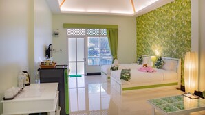 A modern hotel room with a bed, a desk, a glass coffee table, and a view of the city through a large window. - Tubtim Siam River Kwai Resort (Kanchanaburi)