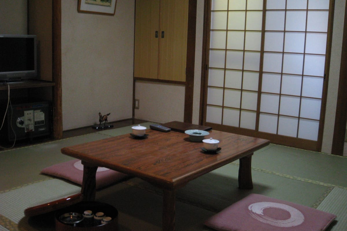 A traditional Japanese room with tatami flooring, a wooden table with dishes, and a sliding door with a grid pattern.