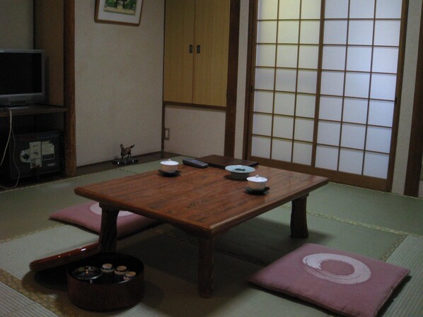 A traditional Japanese room with tatami flooring, a wooden table with dishes, and a sliding door with a grid pattern.