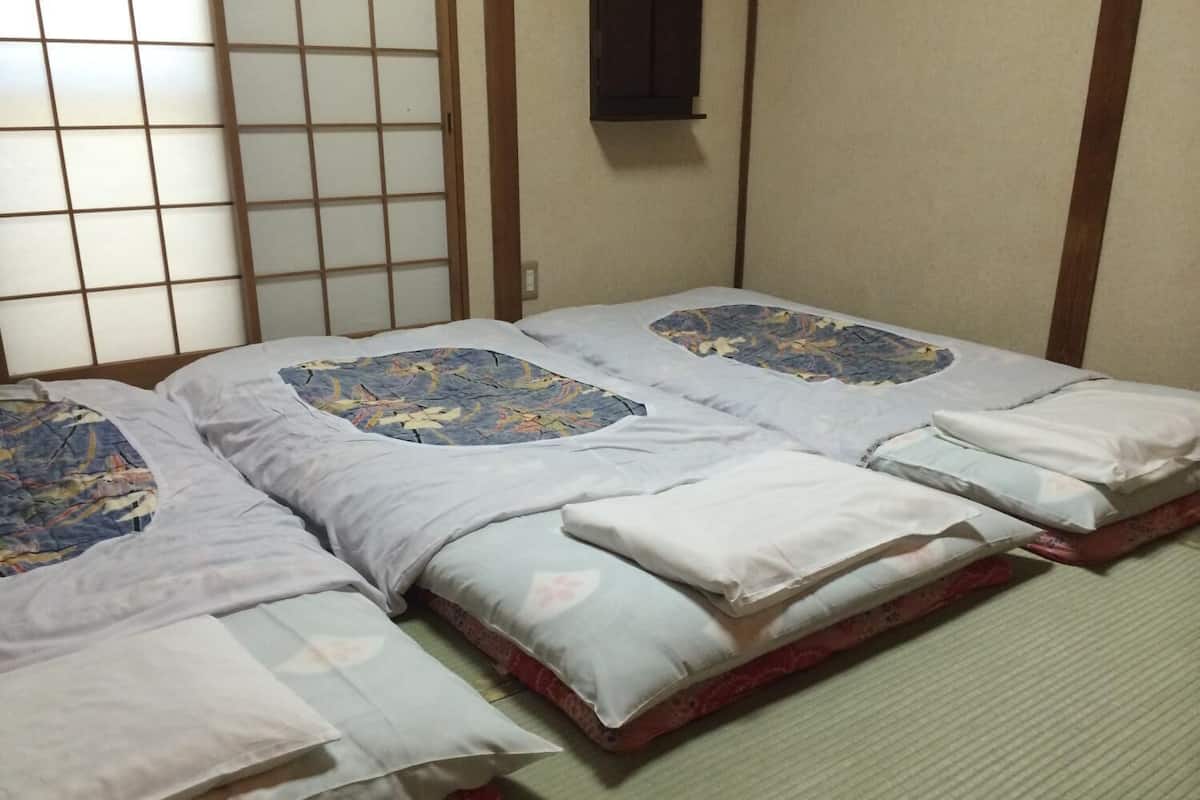 A traditional Japanese room with tatami flooring, a shoji screen, and a futon bed with a patterned cover.