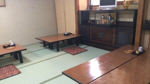 A traditional tatami mat room with low tables and a television on a shelf. - Nihonkan (Kyoto)