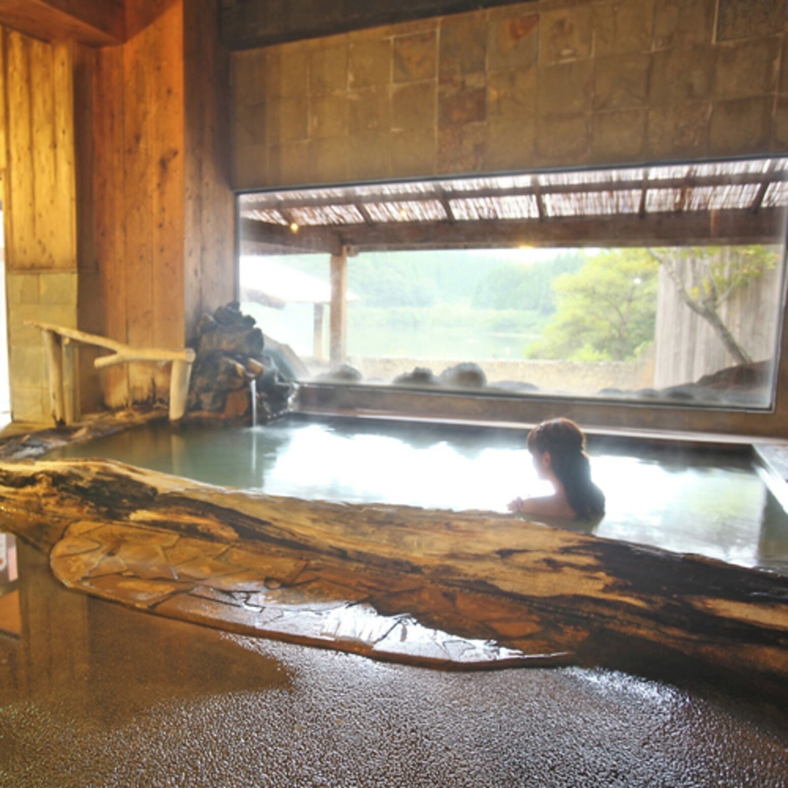 Une cabane en bois avec une grande baignoire en bois remplie d’eau, un banc en bois et un intérieur rustique.