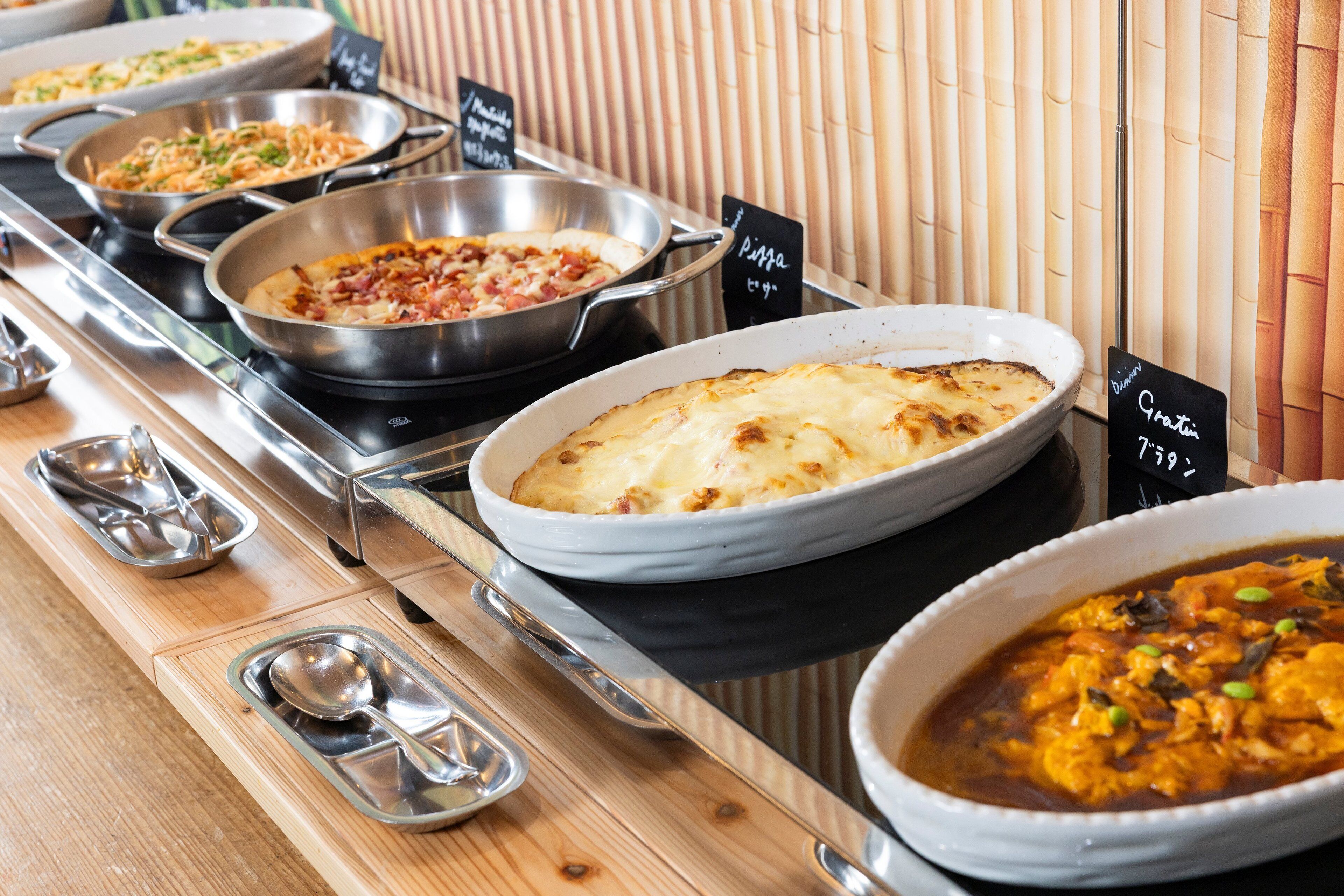 Un buffet proposant divers plats, notamment des pizzas et un plat de curry, présentés sur une table en bois avec des plats de service en métal.