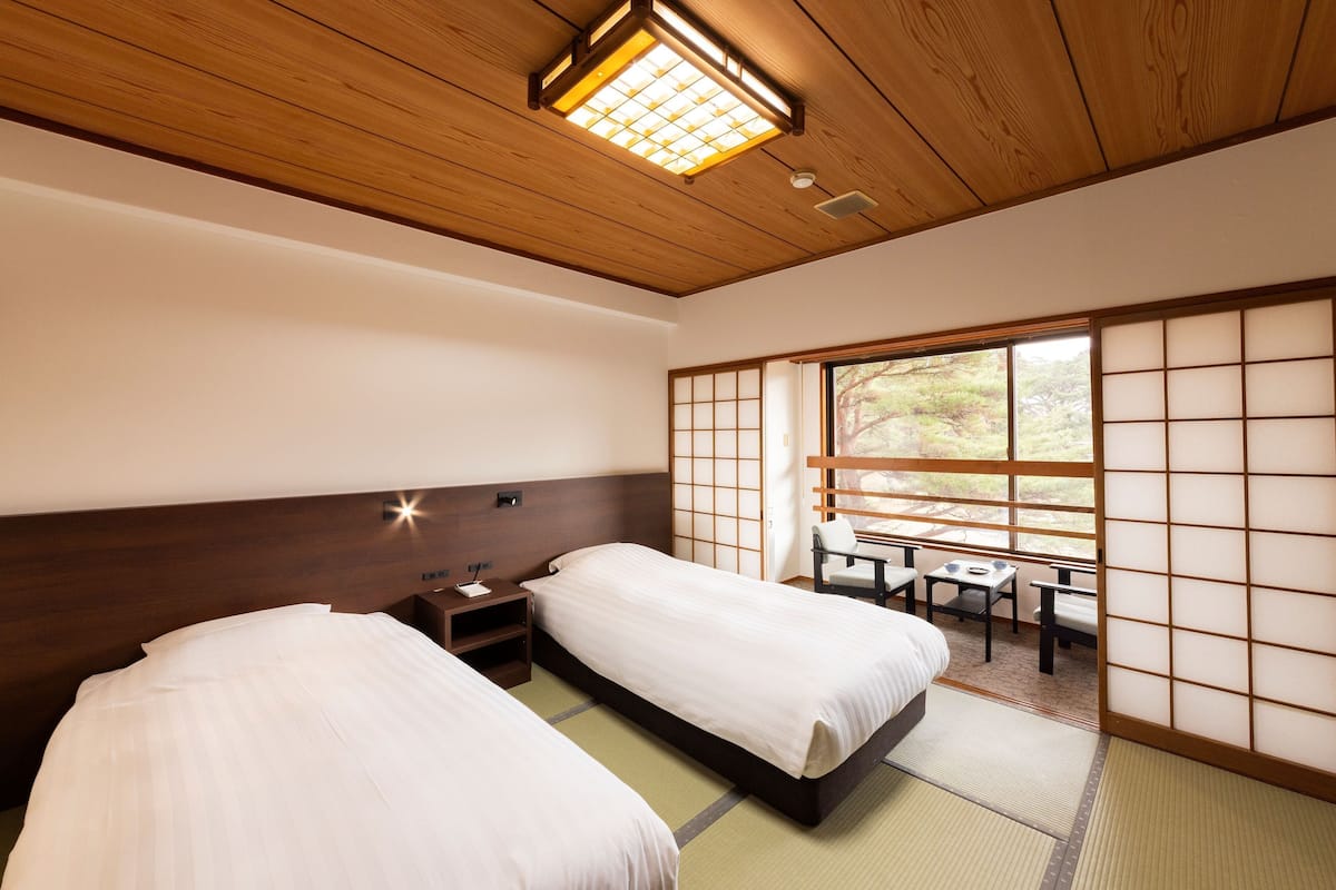 Une pièce de style japonais traditionnel, dotée de deux lits, d’un plafond en bois et offrant une vue sur l’extérieur grâce à des paravents coulissants.