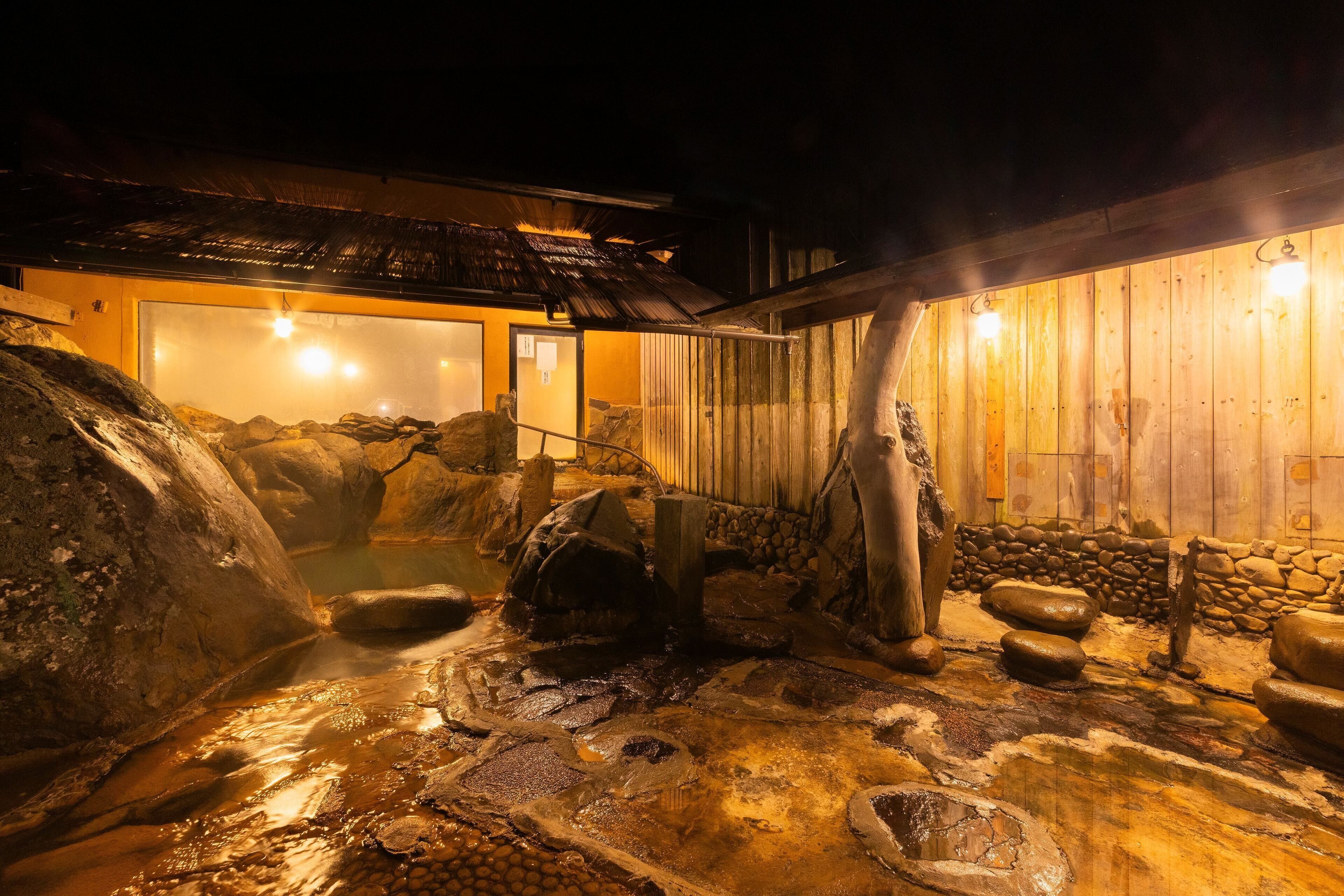 Ein traditionelles japanisches Onsen mit einem Badebereich aus Stein, Holzwänden und einem Reetdach.