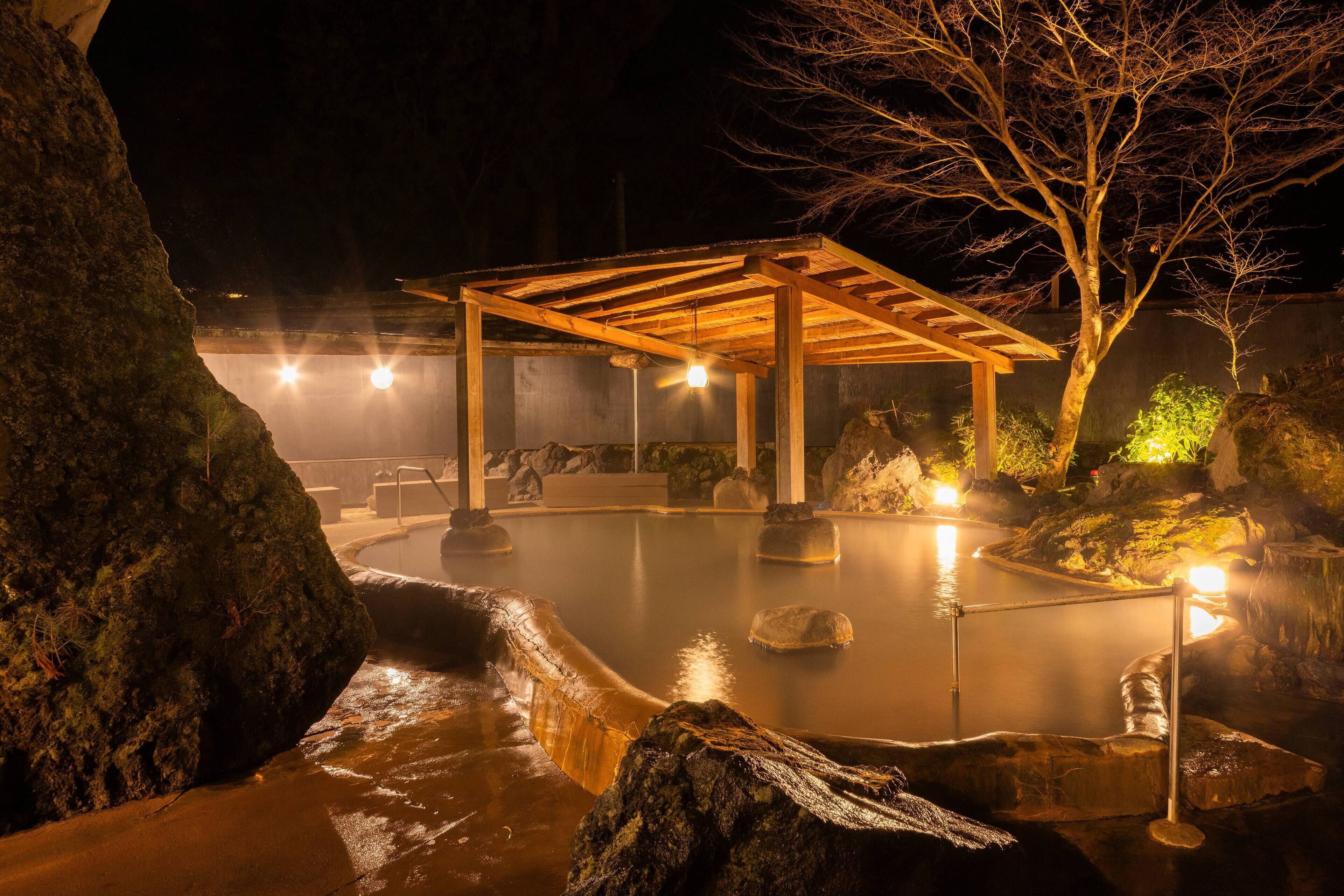 A hot spring area with a wooden pavilion, rocks, and a tree.